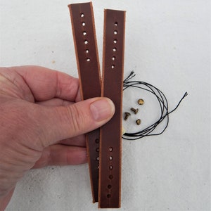 Replacement cut-to-fit belt loops in brown leather here shown in a hand.  Shows two strips of leather with prepunched holes and the rivits and thread, either can be used to make the loop.