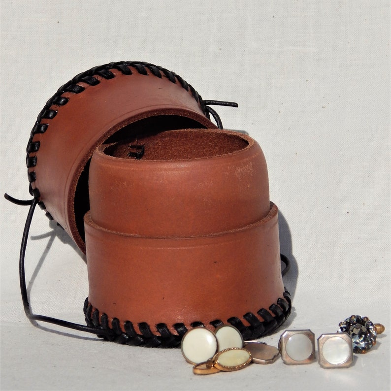 A circular leather pot open with cufflinks and studs (not included) lid that can be used as a second pot.  Vegetable tanned leather with a plait like thonging around the base and top.