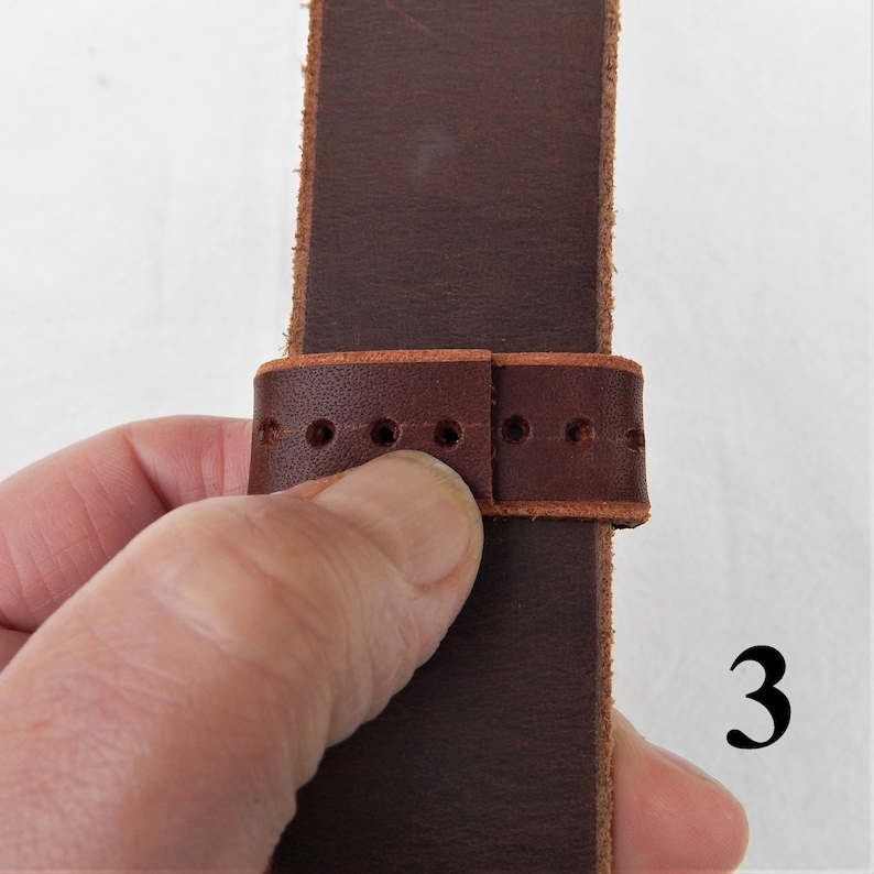 Shown here, step 3 of fitting a replacement belt loop strap keeper, shown in hand.
3. Lay over other side firmly, line up holes and trim, allowing at least one hole overlap.