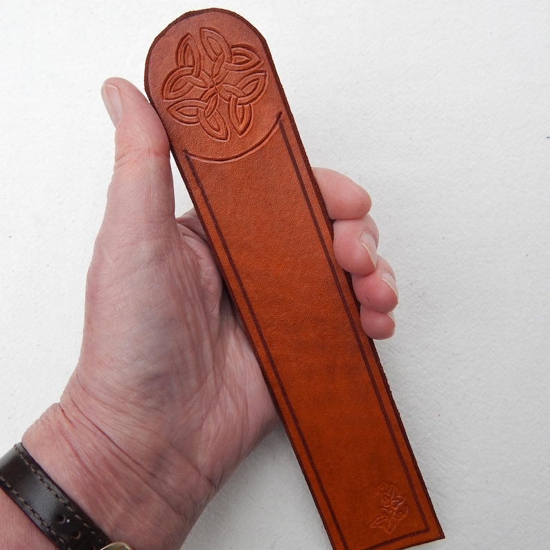 Domed top, natural leather bookmark with embossed celtic knot.  Lightly stained, with a satin finish.  Shown in hand.  Shades will vary.