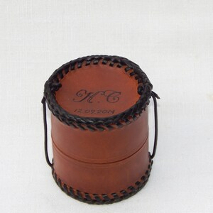 Top of a circular leather pot showing optional personalisation, here with the initials KC and an important date on the lid.  Vegetable tanned leather with a plait like thonging around the base and top, thong is twisted beneath to keep it closed.