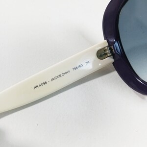 Peut inclure: Gros plan sur des lunettes de soleil avec une monture violette et une branche blanche. Le texte "RA 4098 - JACKIE OHH II 766/8G 3N" est imprim&eacute; sur la branche. Les verres sont bleus d&eacute;grad&eacute;s.