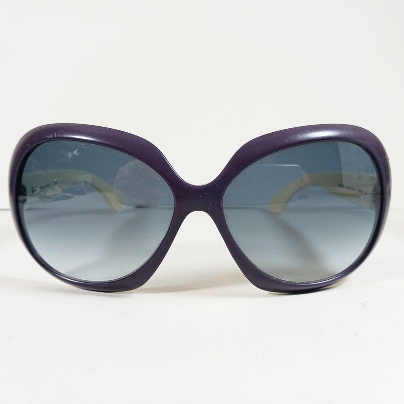 Peut inclure: Lunettes de soleil violettes surdimensionn&eacute;es avec verres d&eacute;grad&eacute;s. Les montures sont violet fonc&eacute;, et les verres passent d'une teinte plus fonc&eacute;e en haut &agrave; une teinte plus claire en bas. Les branches sont jaune clair.