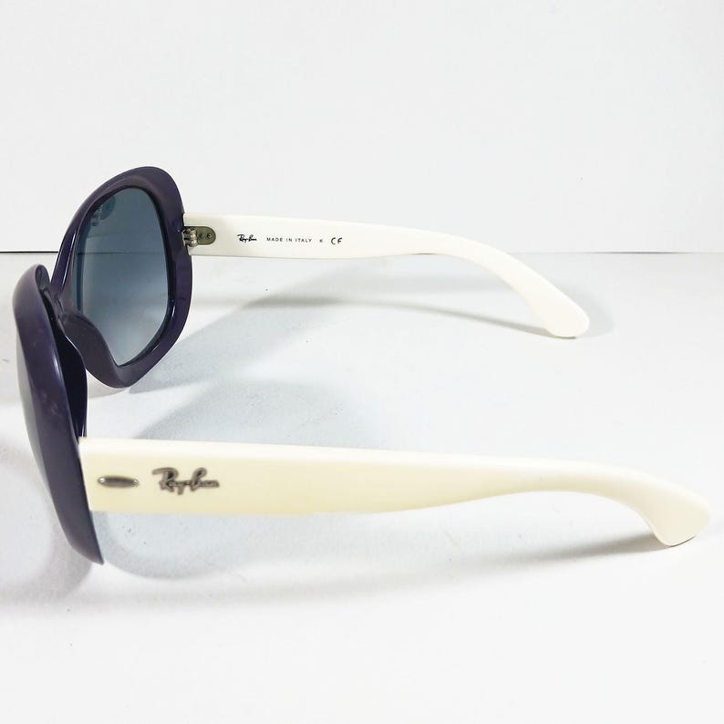 Peut inclure: Lunettes de soleil surdimensionn&eacute;es avec une monture violet fonc&eacute; et des branches blanches. Les verres sont bleu d&eacute;grad&eacute;. Le logo Ray-Ban est visible sur la branche. Fabriqu&eacute; en Italie est imprim&eacute; sur la branche.