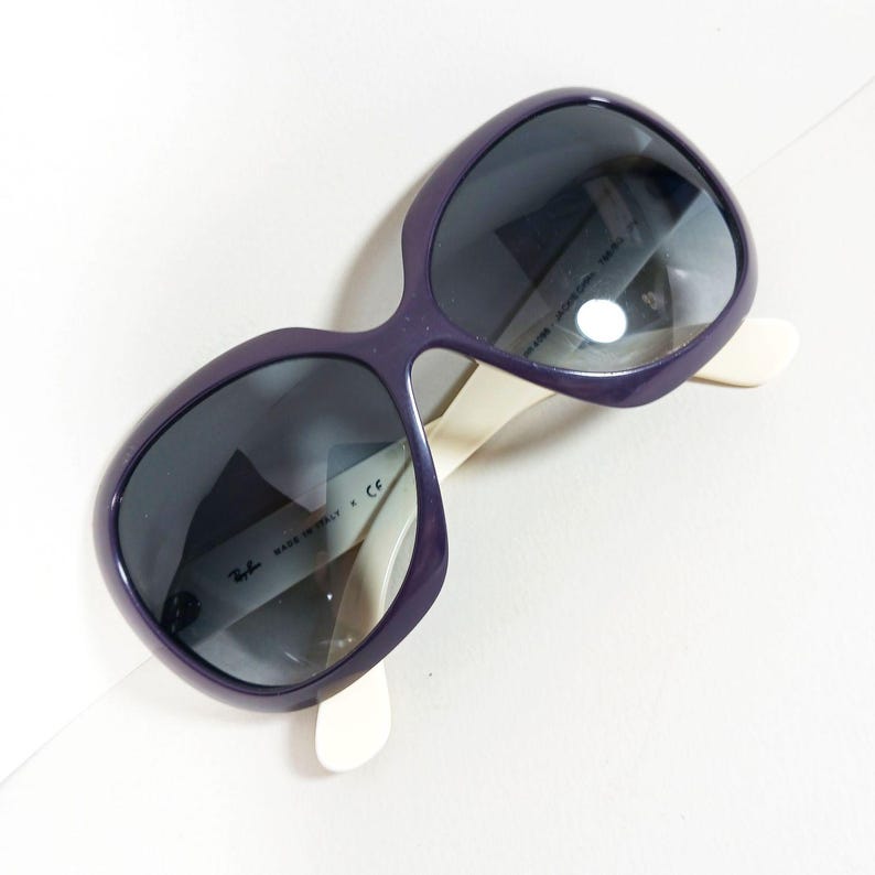 Peut inclure: Lunettes de soleil violettes avec des verres fonc&eacute;s et des branches blanc cass&eacute;. Les lunettes ont une monture arrondie et surdimensionn&eacute;e. Le texte "MADE IN ITALY" et le logo Ray-Ban sont visibles &agrave; l'int&eacute;rieur de la monture.