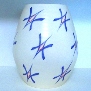 May include: A white ceramic vase with a rounded shape. The vase is decorated with blue starburst designs, each with a red centre. The vase has a smooth, glossy finish and is suitable for displaying flowers or as a decorative item.
