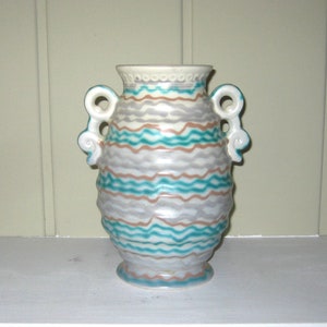 May include: A white ceramic vase with two handles and a wavy pattern in shades of teal, brown, and gray.