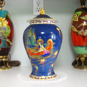 Pode incluir: Três lamparinas decorativas de cerâmica com detalhes dourados e desenhos intrincados. As lamparinas apresentam um esquema de cores azul, vermelho e verde com motivos de pássaros. As lamparinas estão em uma prateleira branca.