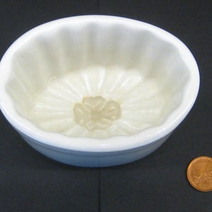 May include: White ceramic mold with a fluted design, used for making jellies or desserts. The mold is oval shaped and has a small, round opening in the center.