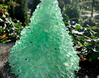 May include: A green glass Christmas tree made of many small pieces of sea glass. The tree is decorated with small, colorful gems. The tree is topped with a white crystal star.