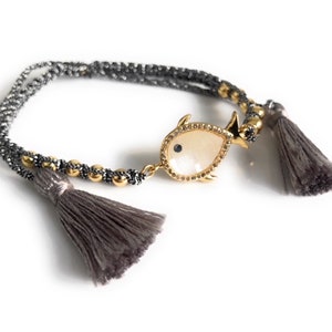May include: A gray and silver beaded bracelet with a gold fish charm and gray tassels.