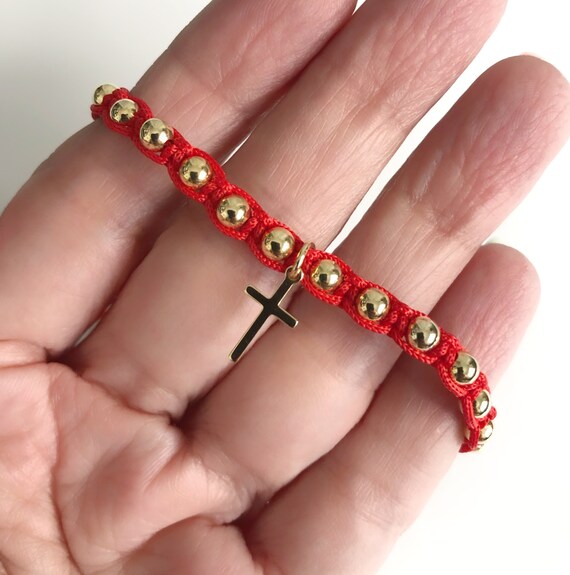 A red string bracelet with a gold-plated cross pendan