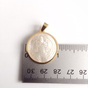 May include: A gold-toned pendant with a white, round, mother-of-pearl inlay featuring a religious figure. The pendant is approximately 2.8 cm in diameter.