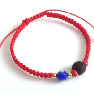 May include: Red string bracelet with a black bead, a blue evil eye bead, and gold beads.