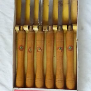 May include: A set of six wood carving chisels in a cardboard box. The chisels have wooden handles with a green and red emblem. The box has the word "MARPLES" in red letters.