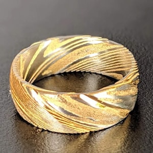 Könnte beinhalten: Ein Ring aus Metall mit einem einzigartigen Wirbelmuster in Gold und Silber. Der Ring hat eine polierte Oberfläche.