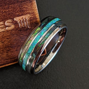 May include: A silver ring with a black and green inlay. The ring is in a wooden box with the text "Pillar Styles" engraved on the box.