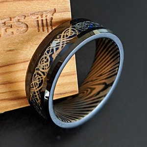 May include: Black and gold wedding band with a Celtic knot design. The band has a brushed finish and a beveled edge.