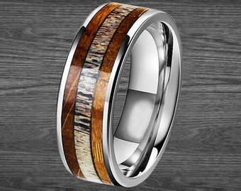 May include: A silver ring with a wood inlay. The ring features a polished silver band with a center inlay of light and dark brown wood grain. The ring is a close-up shot against a dark wood grain background. The text "PILLAR STYLES" is at the bottom.