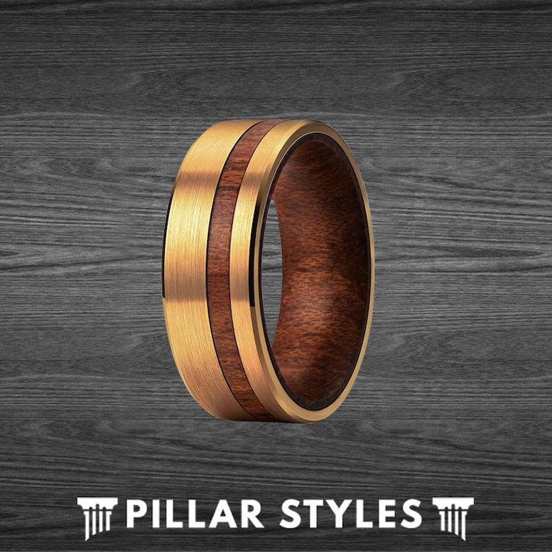 May include: A gold and brown wedding band with a wood inlay. The band is made of tungsten carbide and features a brushed finish.
