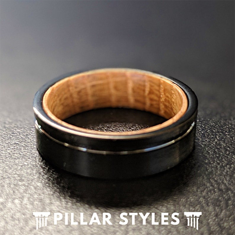 May include: A black tungsten carbide ring with a wood inlay. The ring has a beveled edge and a polished finish.