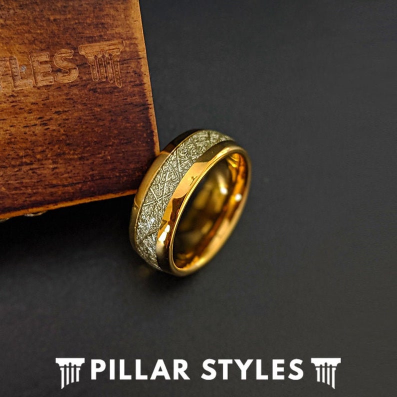 May include: A gold tungsten carbide ring with a meteorite inlay. The ring has a polished finish and a comfortable fit.