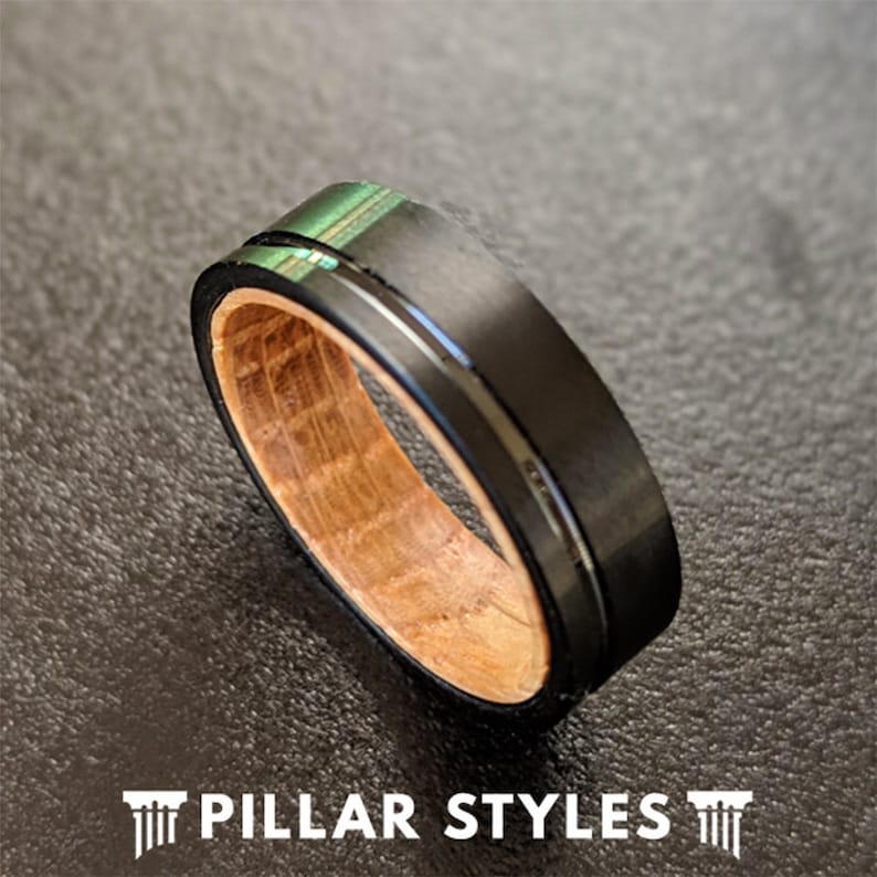 May include: A black tungsten carbide ring with a wood inlay and a silver band. The ring has a green iridescent finish.
