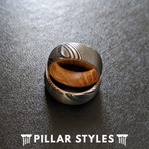 May include: Two stacked rings with a wood inlay and a patterned metal exterior. The rings are silver and black with a wood grain pattern.