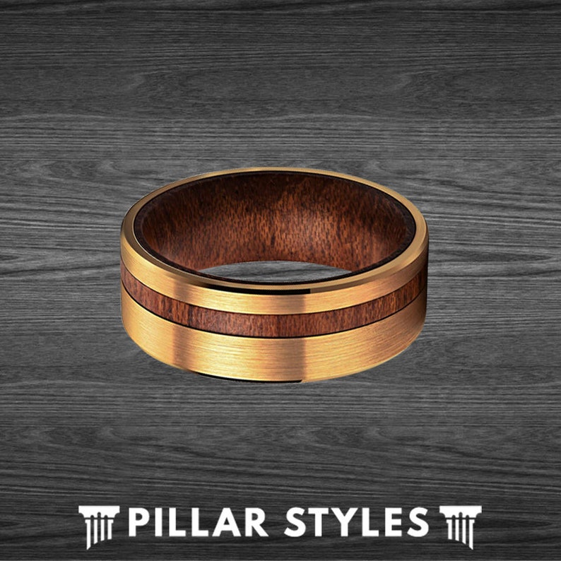 May include: A gold tungsten carbide ring with a brown wood inlay. The ring has a brushed finish and a polished edge.