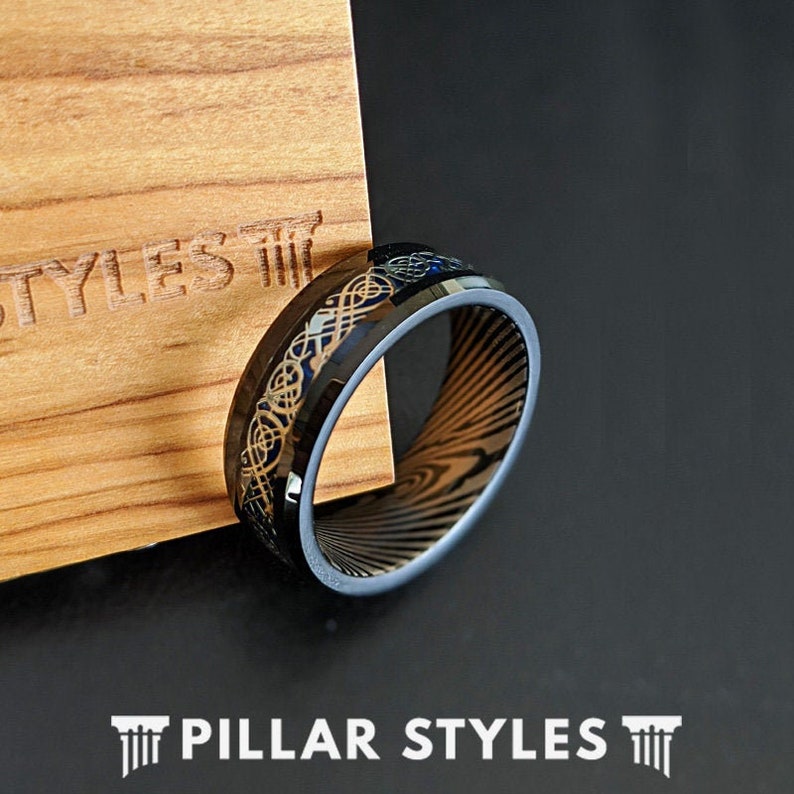 May include: Black and gold wedding band with a Celtic knot design. The band has a brushed finish and a beveled edge.
