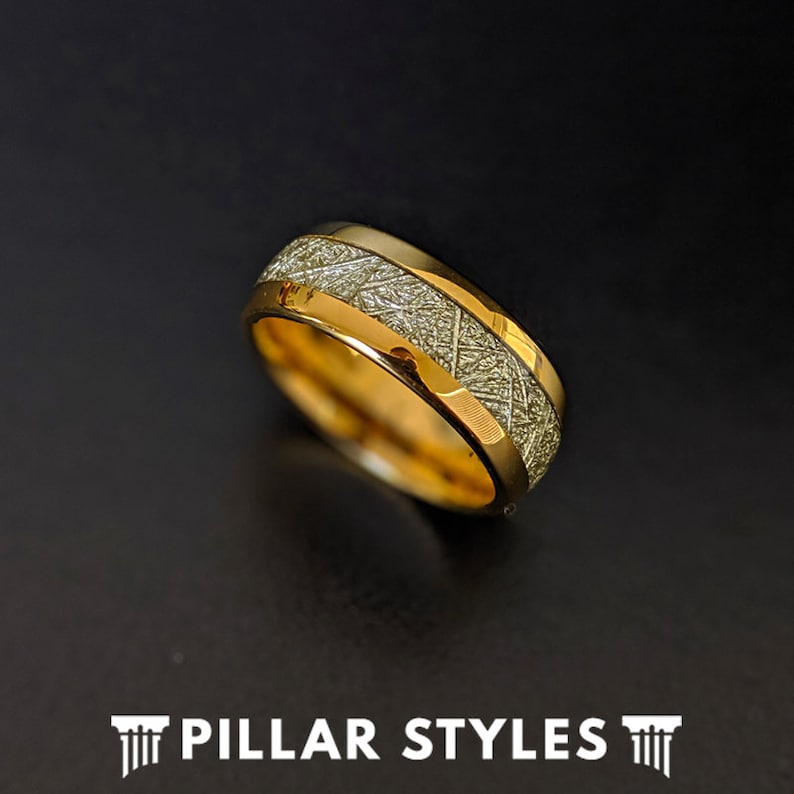 May include: A gold wedding band with a meteorite inlay. The band has a polished finish and a comfortable fit.