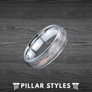 May include: A silver wedding band with a brushed finish and a rose gold arrow design. The arrow is set into a groove in the band and has a textured finish.
