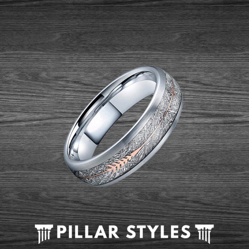 May include: A silver wedding band with a brushed finish and a rose gold arrow design. The arrow is set into a groove in the band and has a textured finish.