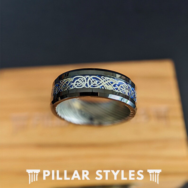 May include: A black tungsten carbide ring with a blue inlay and a silver Celtic knot design.