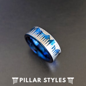 May include: A blue tungsten carbide ring with a silver mountain and forest design engraved on the band.