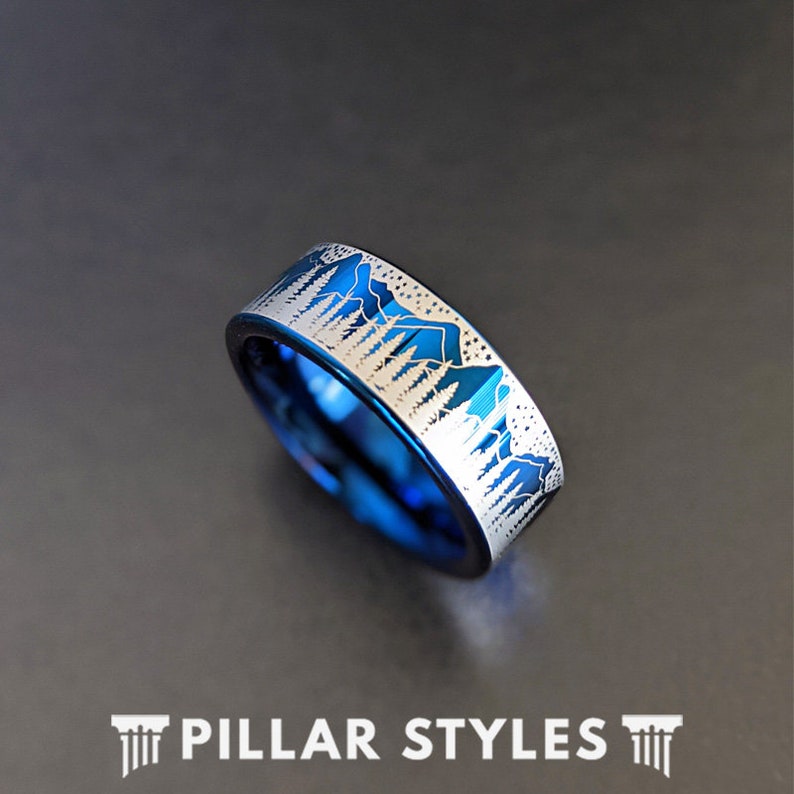 May include: A blue tungsten carbide ring with a silver mountain and forest design engraved on the band.