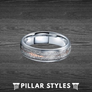 May include: A silver wedding band with a brushed finish and a rose gold arrow design. The band has a textured surface.
