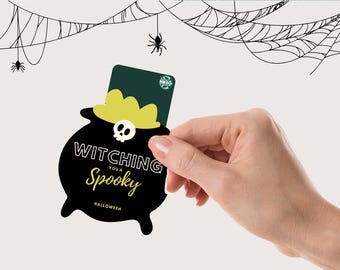 May include: A Halloween-themed gift card held by a hand. The card is in a black cauldron shape with the words "Witching You a Spooky" and a skull. A Starbucks gift card is visible. Spiderwebs and spiders are in the background.