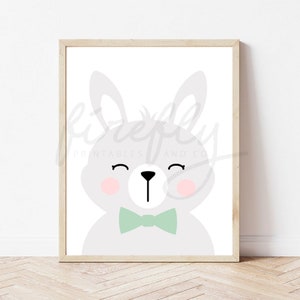 Puede incluir: Un diseño de arte de pared imprimible con un lindo conejito gris con una pajarita verde. El conejito tiene mejillas rosadas y los ojos cerrados, lo que le da una expresión dulce y juguetona.