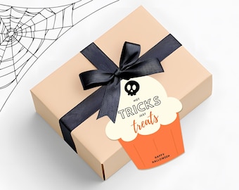 May include: A beige gift box with a black ribbon and bow, adorned with a cupcake-shaped tag. The tag features a skull and the words "Not Tricks Just Treats" in black and orange, with "Happy Halloween" at the bottom.
