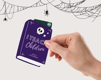 May include: A purple book-shaped gift card holder with the text "I Teach Children" and "Happy Halloween". The holder has a skull and star design. A green gift card is inside. Spiderwebs and spiders are in the background.