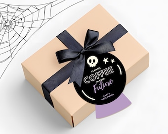 May include: A beige gift box with a black ribbon and bow. A black circular tag with a skull, stars, and the text "I can see coffee in your future" is attached. The words "Happy Halloween" are also on the tag.
