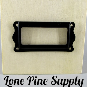 May include: A black metal label holder with a rectangular opening, mounted on a light wood surface. The text "Lone Pine Supply" is printed below the label holder.