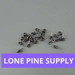 May include: A close-up of a pile of silver-toned metal earring findings. The findings are small and have a loop at the top and a pin at the bottom. The findings are scattered on a gray surface.