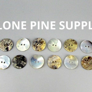 May include: Ten round, two-hole, mother-of-pearl buttons in various shades of brown, beige, and white.