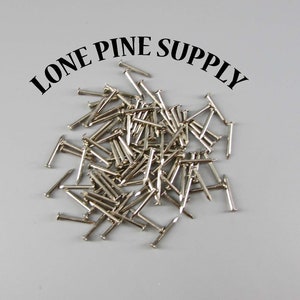 May include: A pile of silver-colored tacks or brads, likely used for crafts or woodworking. The text "LONE PINE SUPPLY" is visible above the tacks.