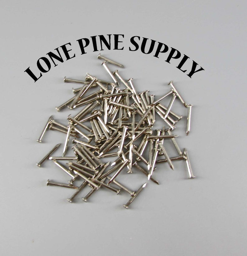 May include: A pile of silver-colored tacks or brads, likely used for crafts or woodworking. The text "LONE PINE SUPPLY" is visible above the tacks.