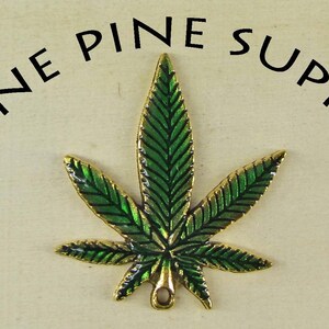 May include: A green and gold metal marijuana leaf charm with a loop for hanging. Lone Pine Supply is written around the leaf.