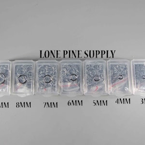 May include: A clear plastic container with seven compartments, each containing a different size of jump rings. The compartments are labeled with the ring size in millimeters: 10 mm, 8 mm, 7 mm, 6 mm, 5 mm, 4 mm, and 3 mm. The container is labeled "LONE PINE SUPPLY".