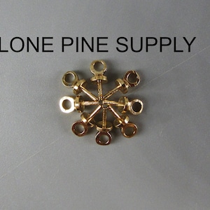 May include: A close-up of a group of eight gold-colored metal eyelets with a small loop on each eyelet. The eyelets are arranged in a circular pattern.